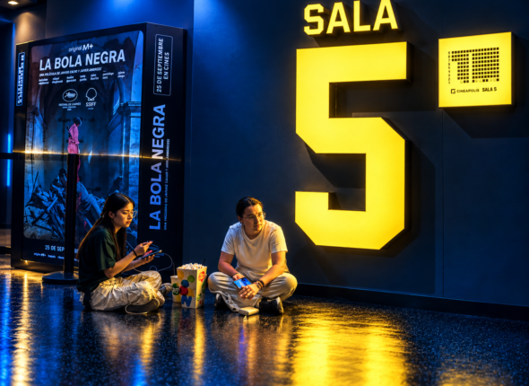 Dos personas sentadas en el suelo de un cine junto a un gran número 5 amarillo, con iluminación azul y amarilla